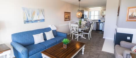 A living room with a blue sofa, a wooden coffee table, and a dining area with white chairs.