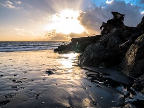 Una playa con rocas y olas, con el sol poniéndose al fondo.