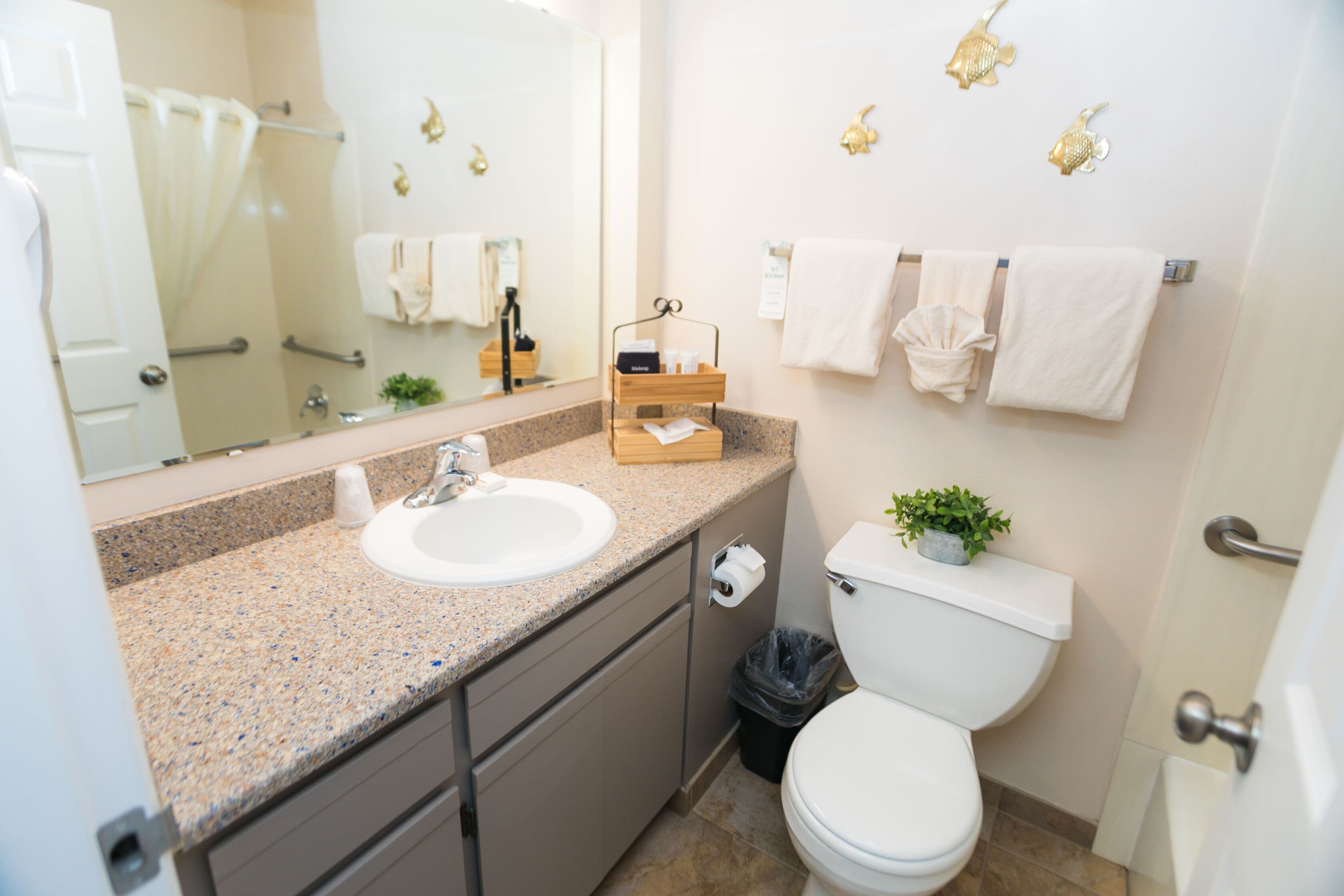Ein modernes Badezimmer mit einer Granittafel, einem weißen Waschbecken, einer Toilette und einem Spiegel. Handtücher hängen an der Wand und auf der Toilette steht eine kleine Pflanze.