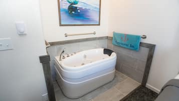 Ein Badezimmer mit einer großen Badewanne, einem Handtuchhalter mit Handtuch, einem Bild an der Wand und einer Haltestange.