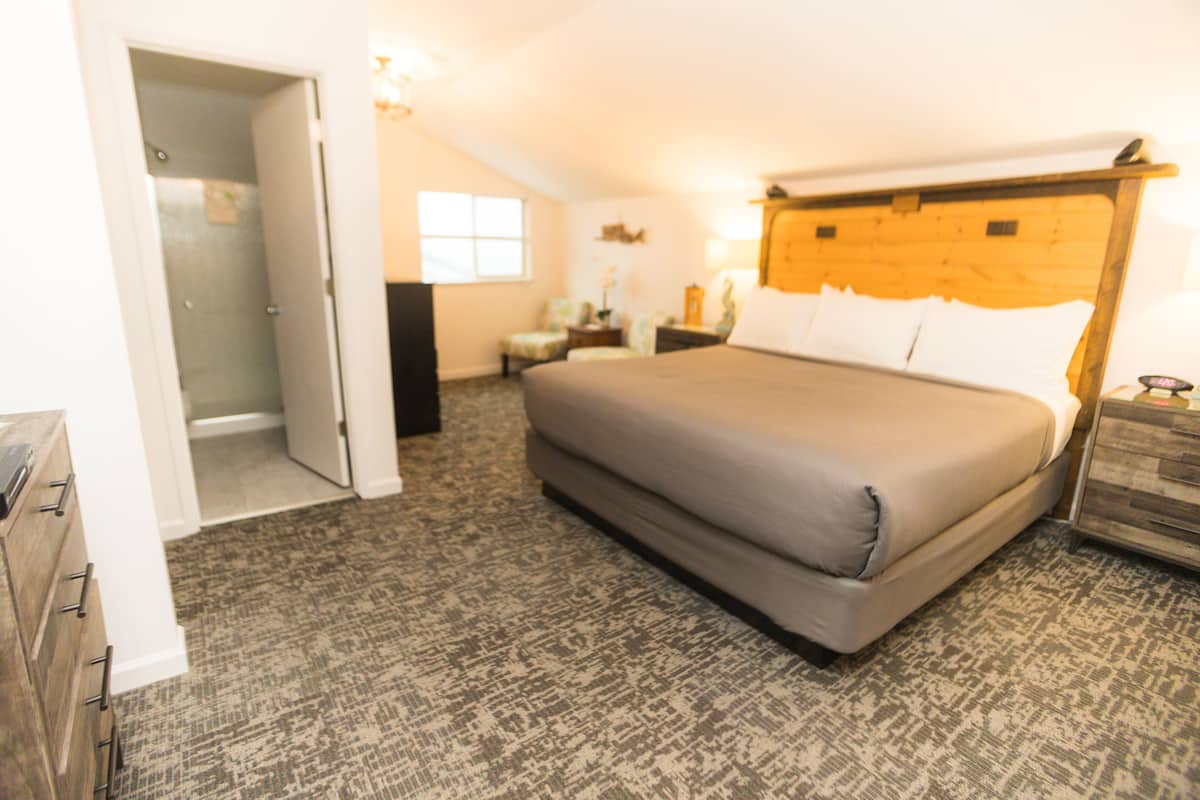 Un dormitorio con una cama grande, un cabecero de madera, una mesita de noche, un aparador, una silla y una pequeña mesa con una lámpara.