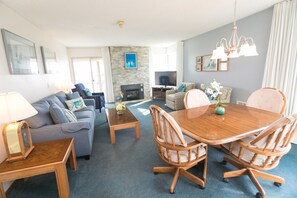 A living room with a sofa, coffee table, dining table, chairs, TV, fireplace, and artwork on the walls. - The Canterbury Inn (Ocean Shores)