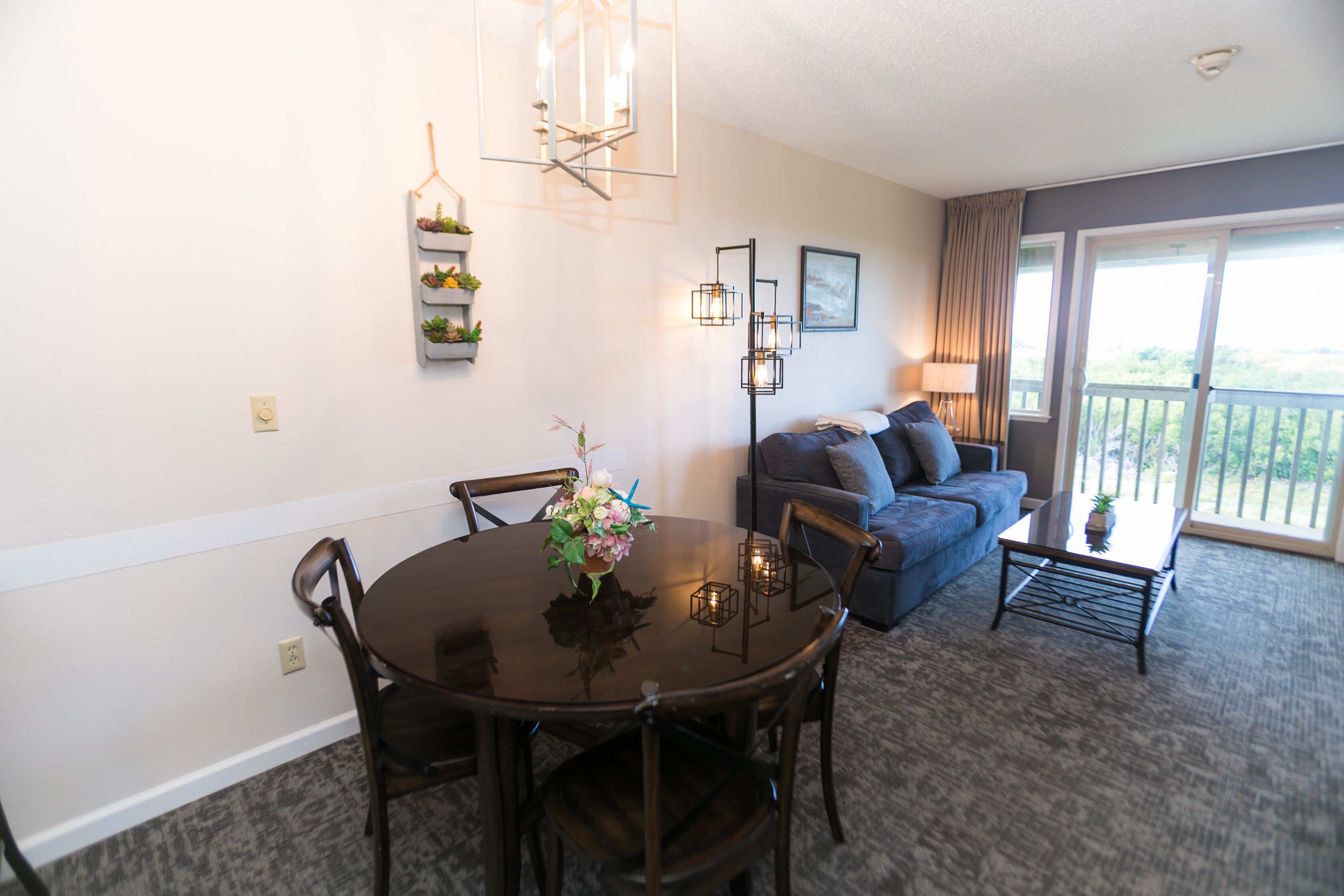A dining area with a round table and chairs, a sofa, and a balcony with a view.