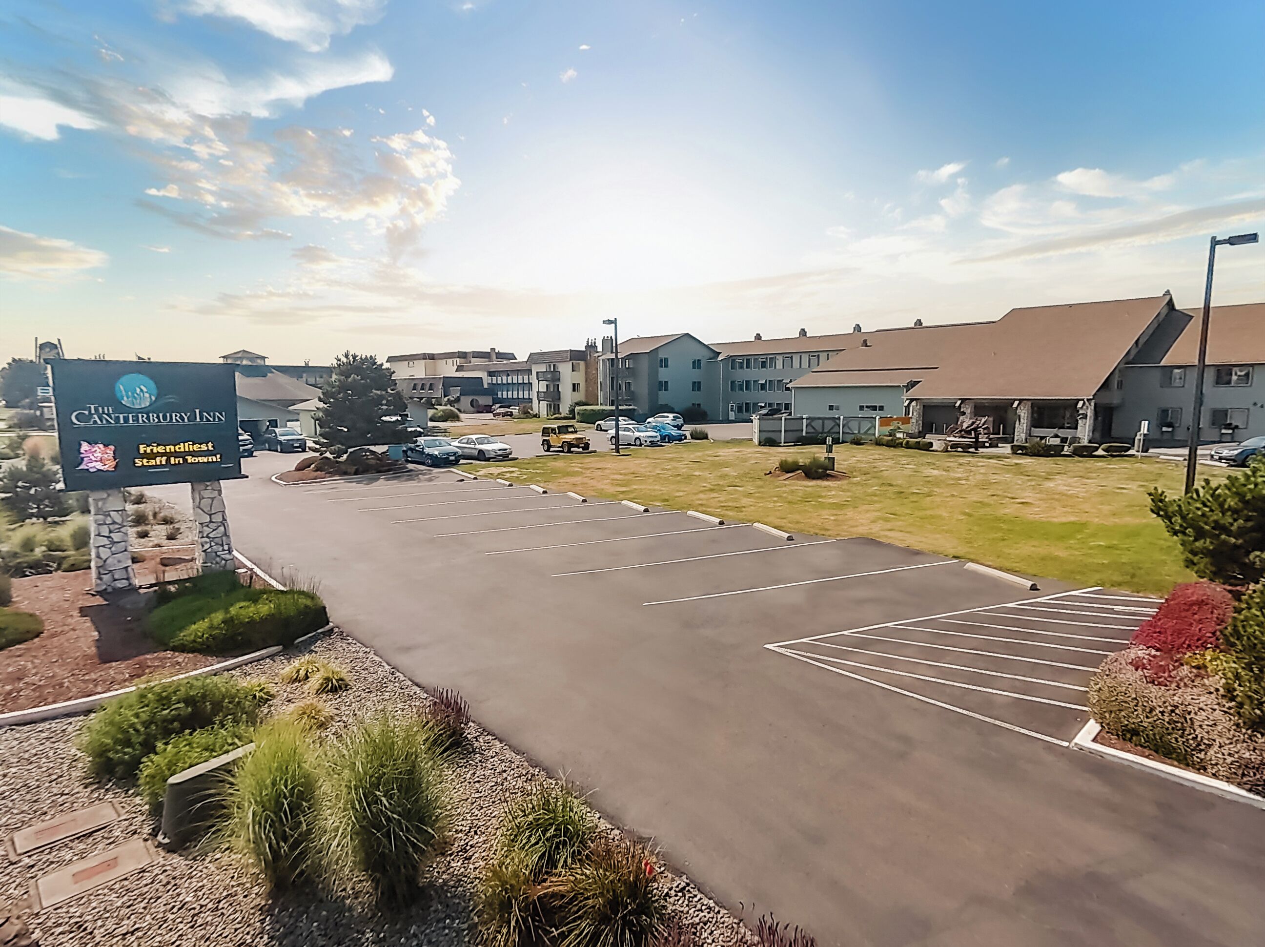 A parking lot with a sign for The Canterbury Inn, a building with a flat roof, and a clear sky.