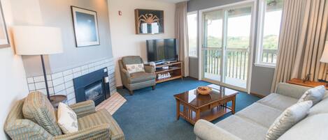 A living room with a fireplace, a television, a sofa, a chair, and a balcony with a view.