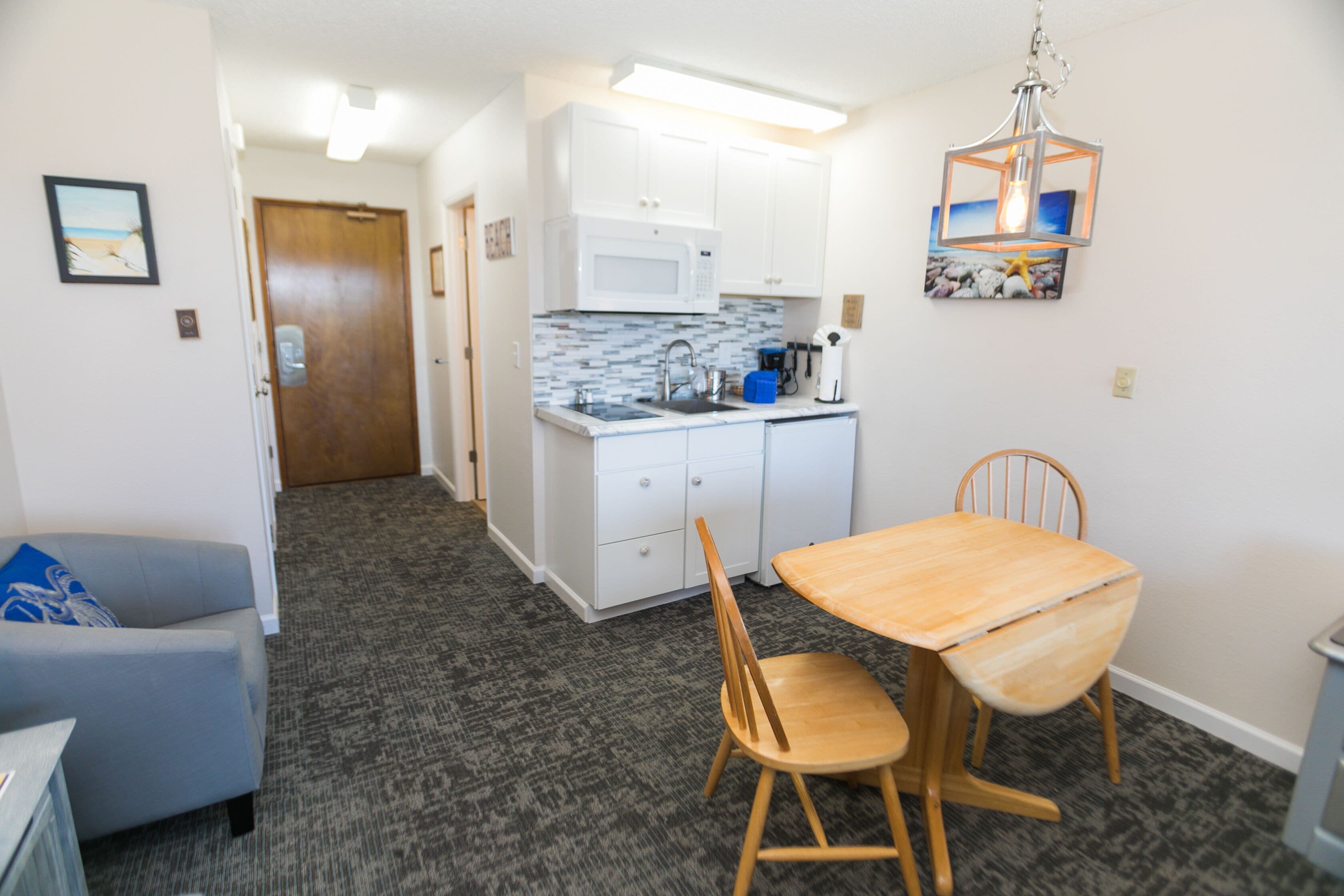 A compact kitchen with white cabinets, a microwave, and a sink. There's a dining area with a wooden table and chairs.