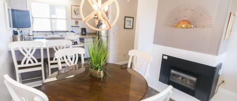 Un coin repas avec une table ronde en bois, des chaises blanches, un luminaire suspendu et une cheminée.