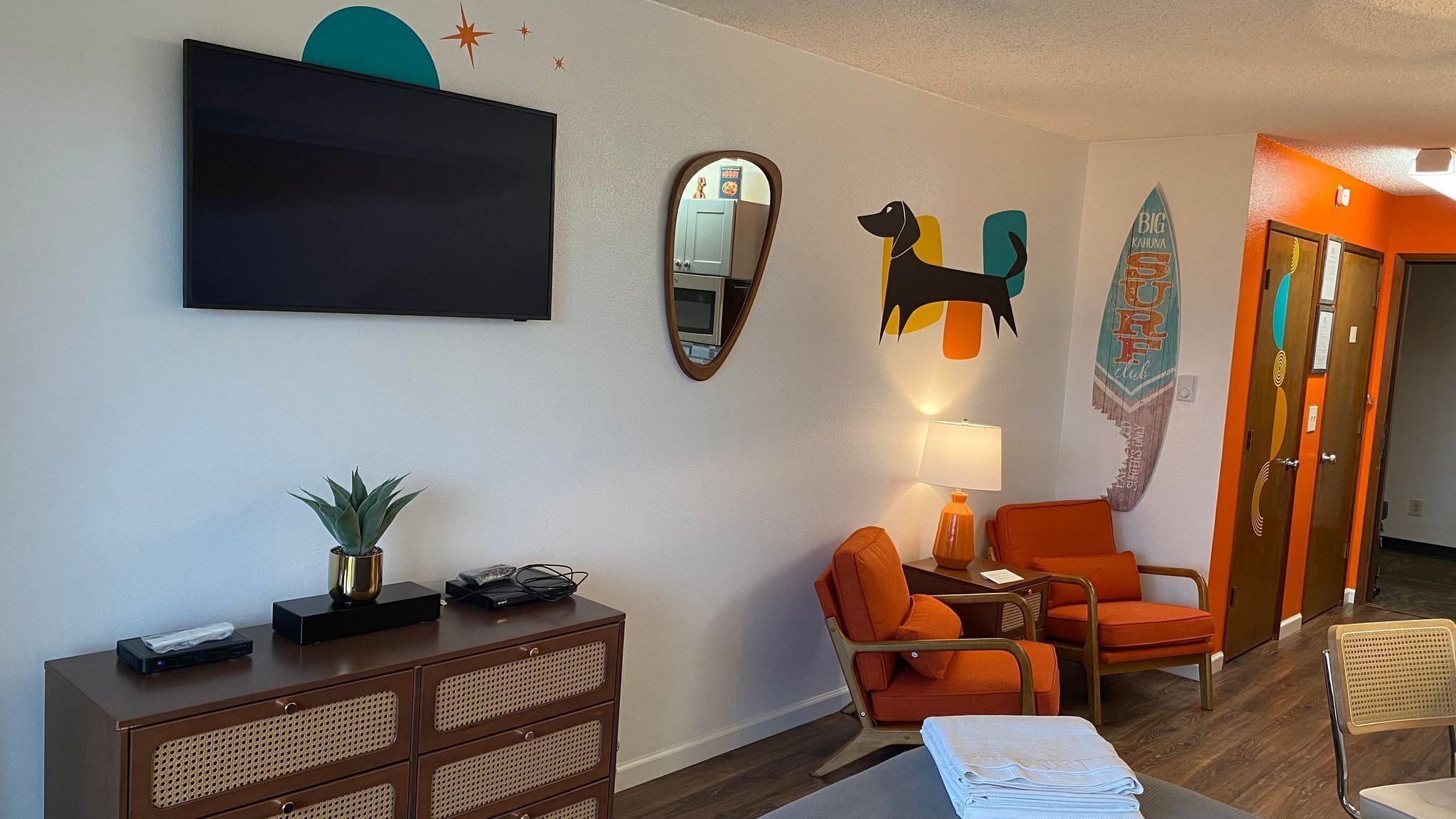A modern living room with a flat-screen TV, a mirror, a dog cutout, and a surfboard decoration.