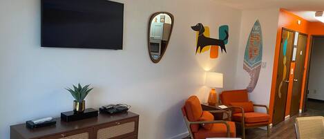 A modern living room with a flat-screen TV, a mirror, a dog cutout, and a surfboard decoration.