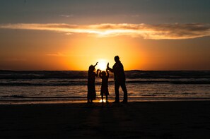 A silhouette of a family against a sunset at the beach. - The Canterbury Inn (Ocean Shores)