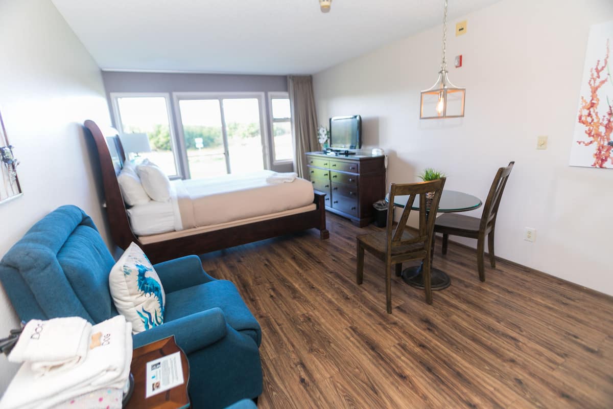 Un dormitorio con cama, cómoda, televisor, mesa de comedor con sillas y ventana con vistas.