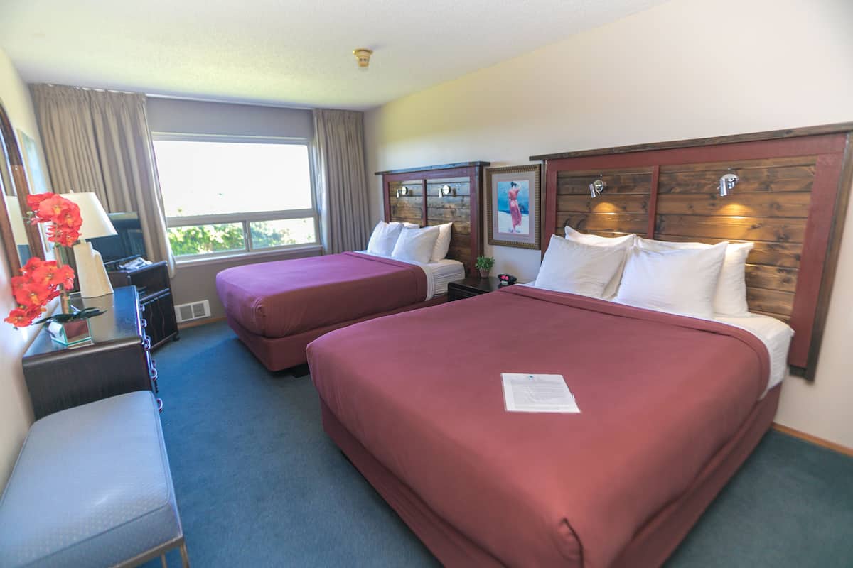 Habitación de hotel con dos camas, un escritorio con lámpara, una silla y una ventana con cortinas.