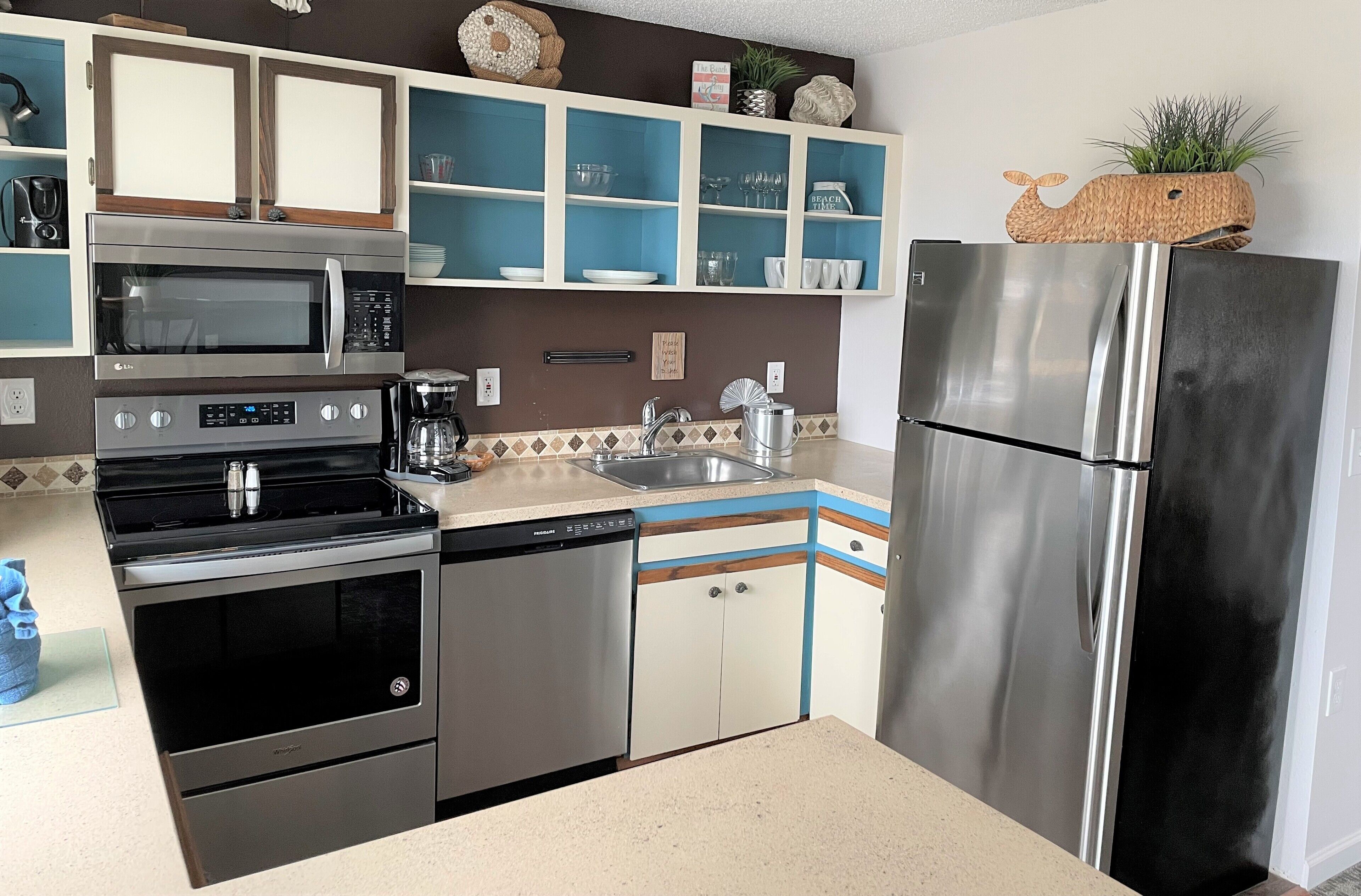 A modern kitchen with stainless steel appliances, blue and white cabinetry, and decorative items on shelves.