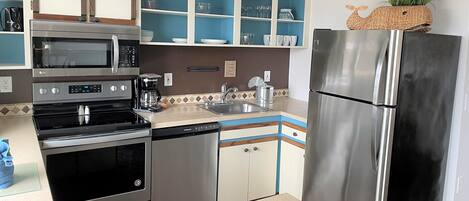 A modern kitchen with stainless steel appliances, blue and white cabinetry, and decorative items on shelves.