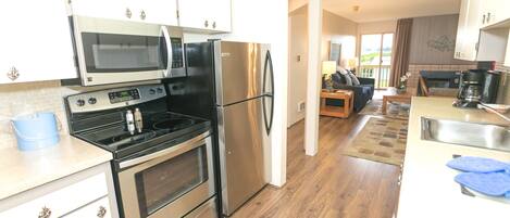 A modern kitchen with stainless steel appliances, wooden flooring, and a view to the living area.