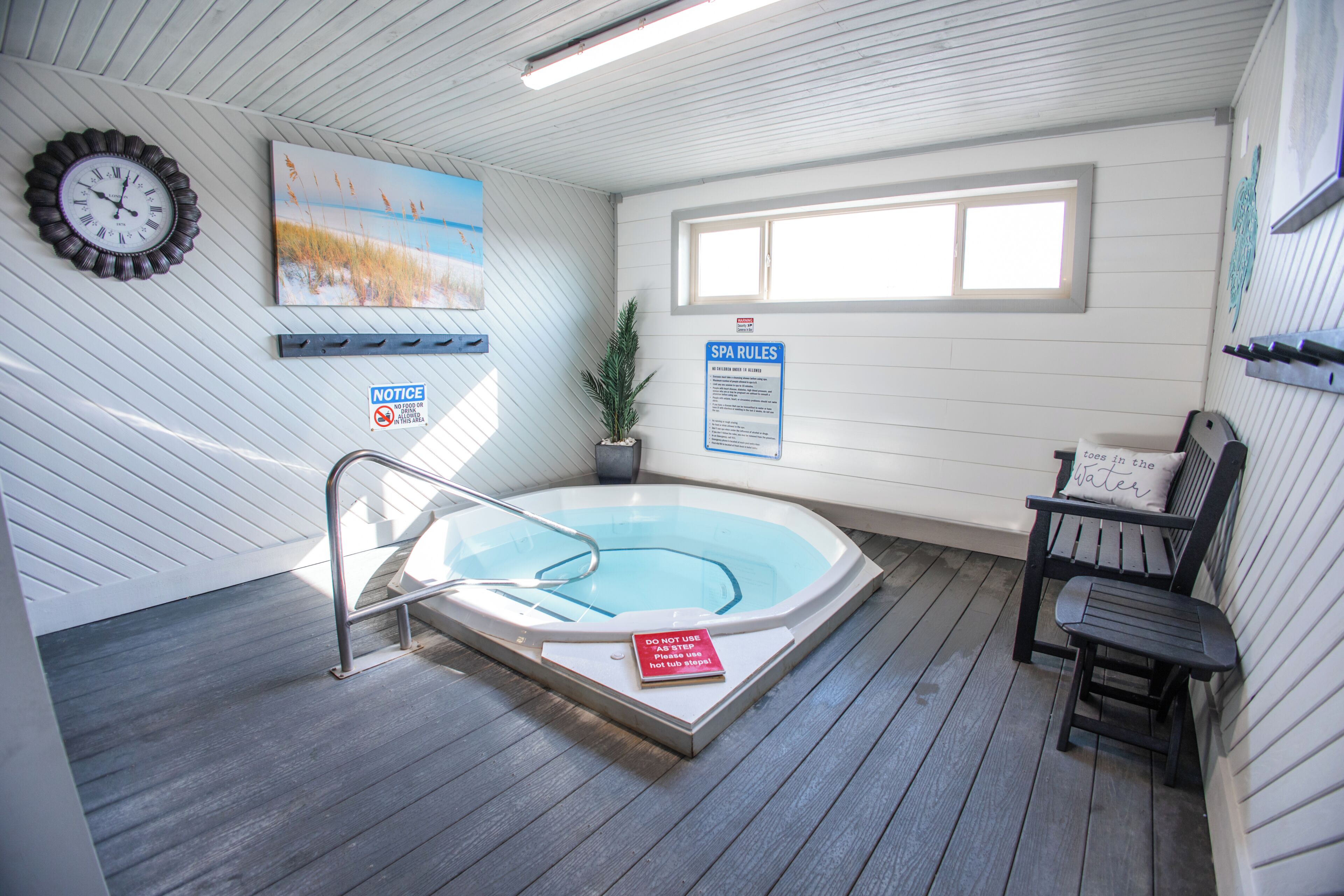 Un área de spa con un jacuzzi, un reloj, un cuadro, una ventana y una silla.