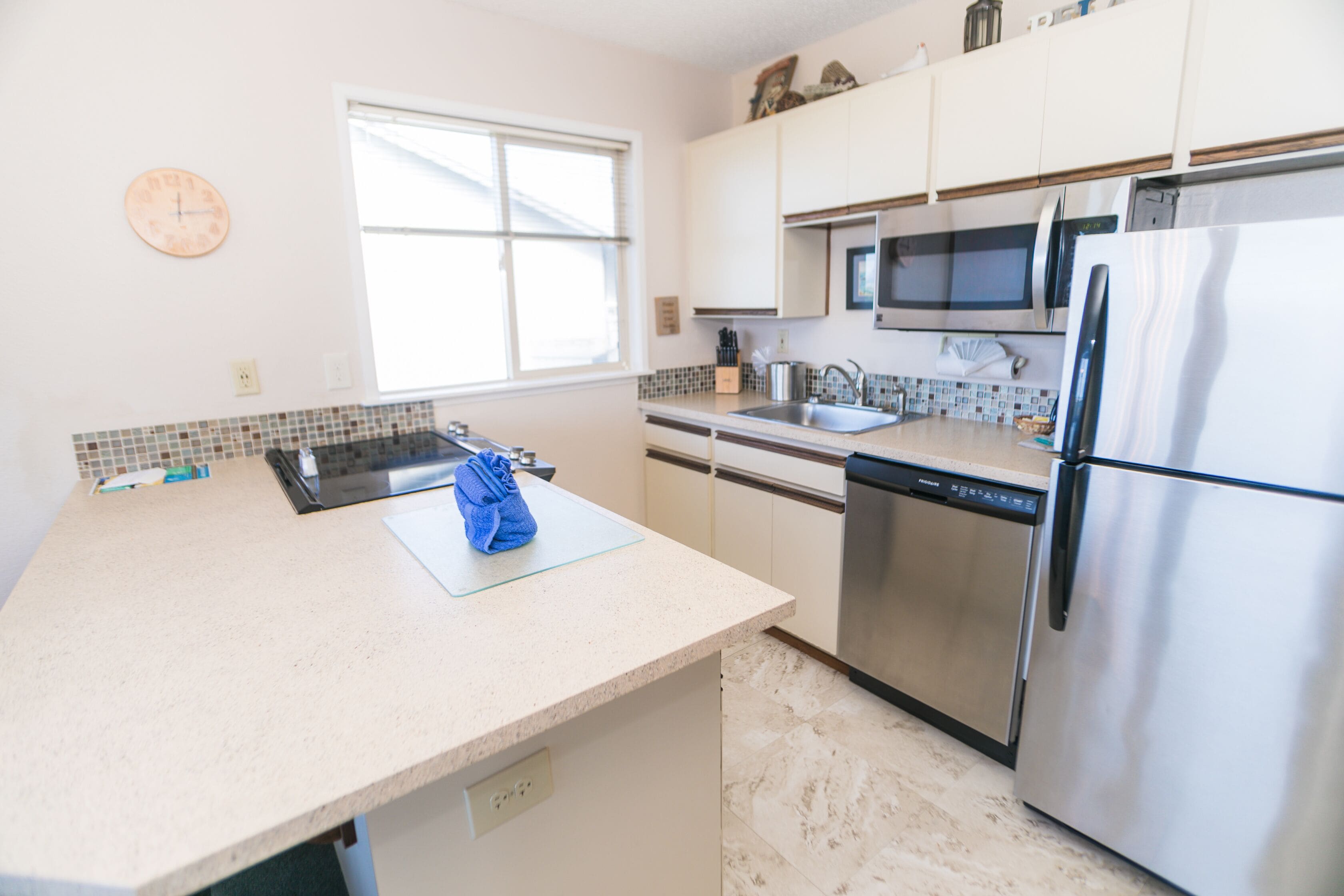 A kitchen with a microwave, refrigerator, dishwasher, and a window with blinds.