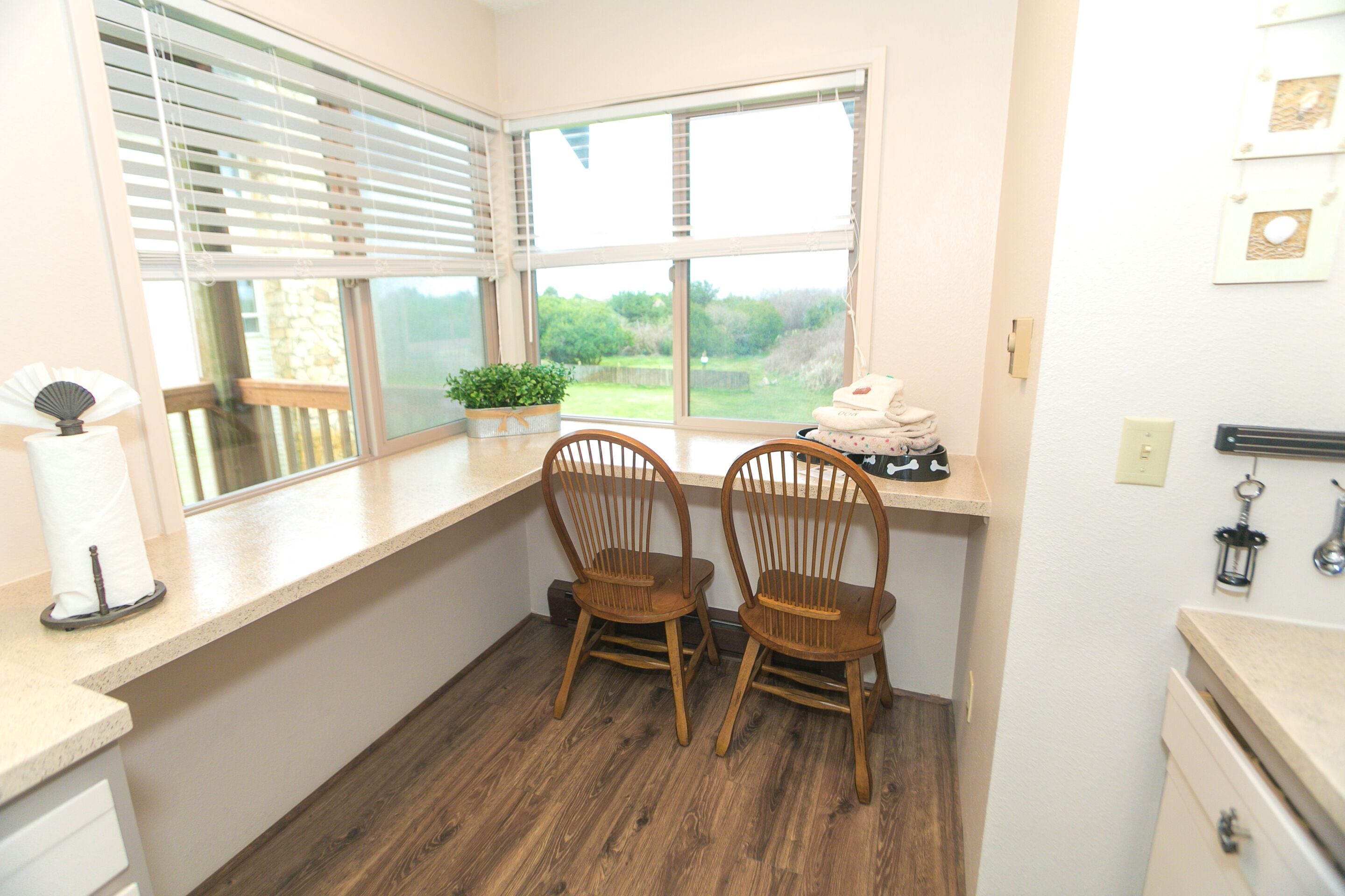 A bathroom with wooden flooring, a window with blinds, two wooden chairs, a towel rack, and a small plant.