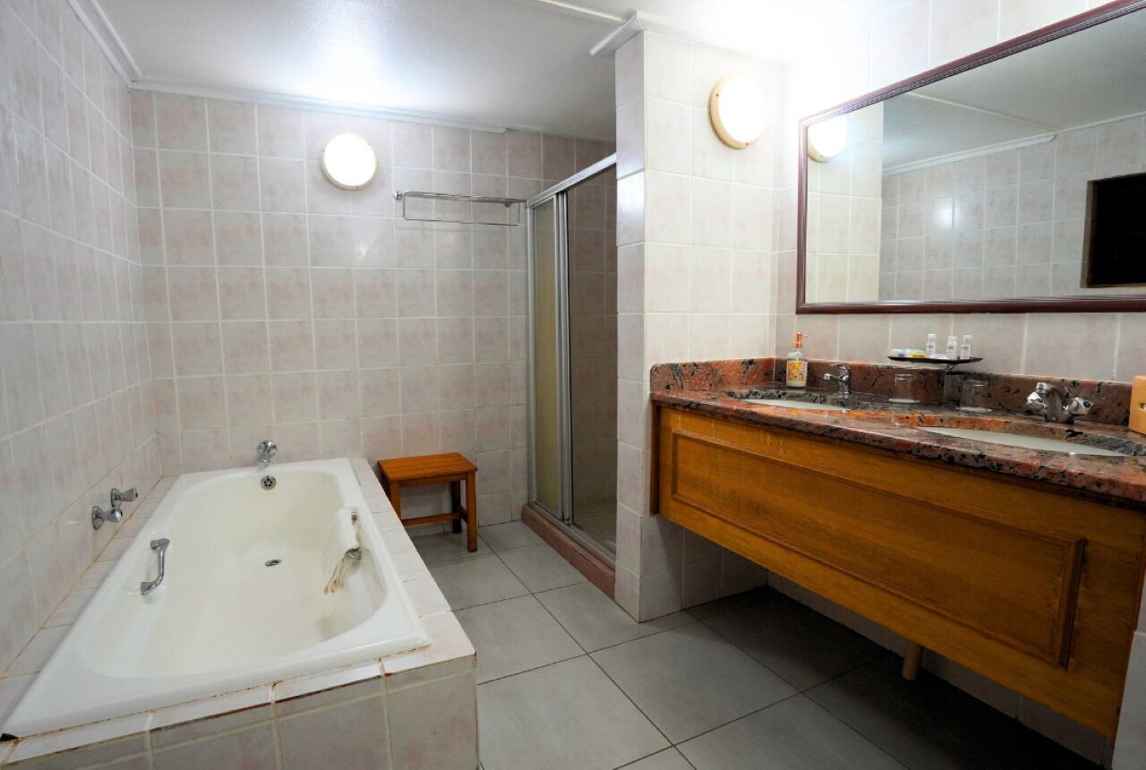 Un baño con bañera, ducha, tocador de madera con lavabo y un espejo grande.