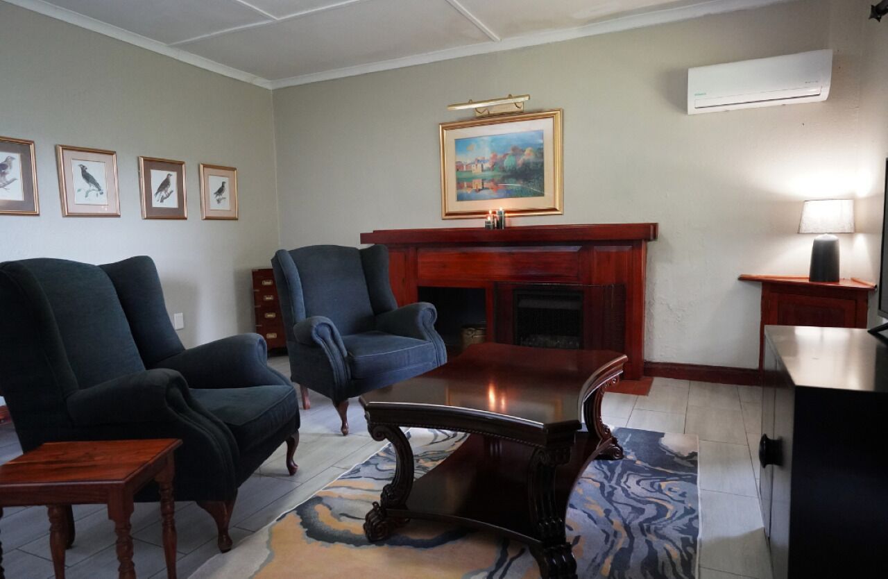 Una sala de estar con dos sillones oscuros, una mesa de centro de madera, una chimenea y un cuadro colgado sobre ella.