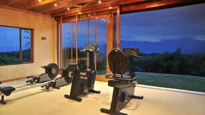 A gym with cardio machines and a view of mountains through large windows. - Coach House Hotel & Spa (Tzaneen)