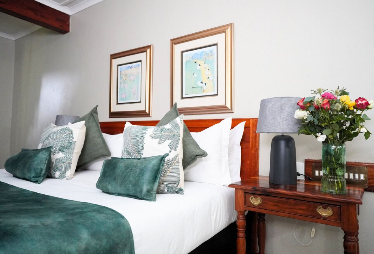 A neatly made bed with green and white bedding, a wooden nightstand with a lamp and vase of flowers, and two framed pictures on the wall.