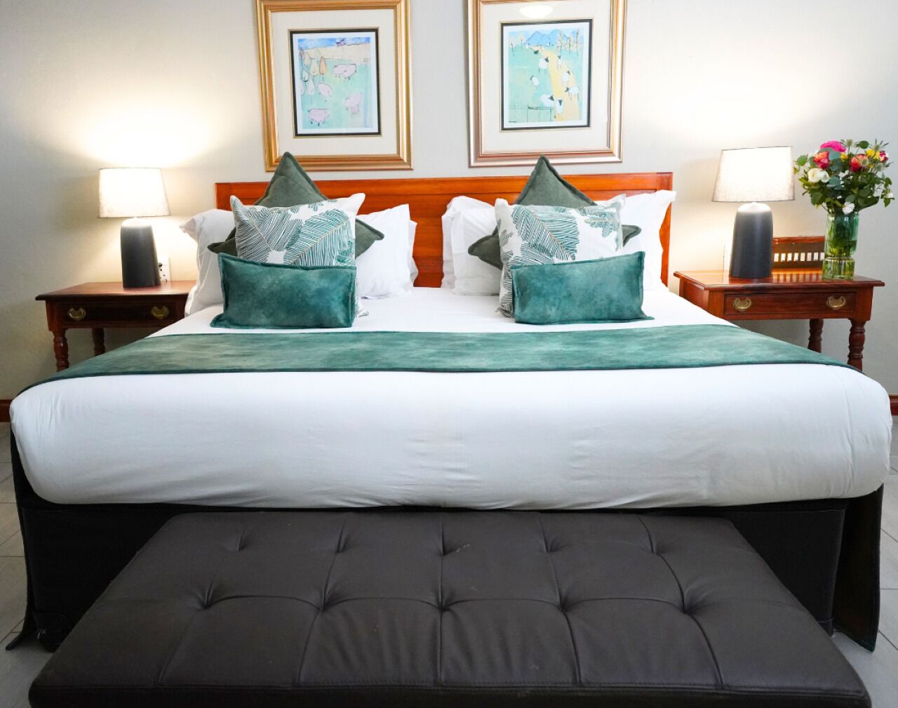 Una cama bien hecha con una manta verde, dos almohadas con motivos de hojas y un banco a juego al pie de la cama.