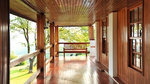 A wooden corridor with a bench, large windows, and a view of greenery. - Coach House Hotel & Spa (Tzaneen)