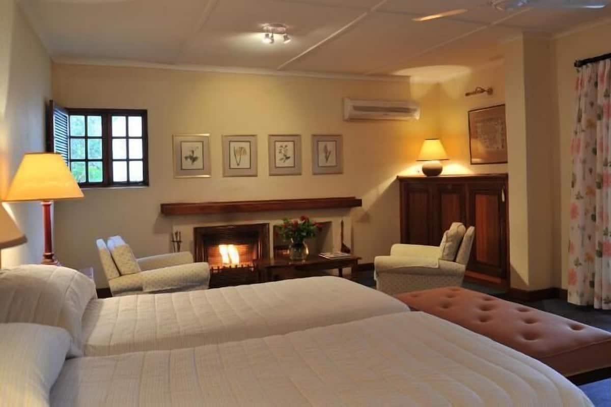 Ein Hotelzimmer mit zwei Betten, einem Kamin, einer Sitzecke mit Sesseln und einem großen Fenster mit Vorhängen.