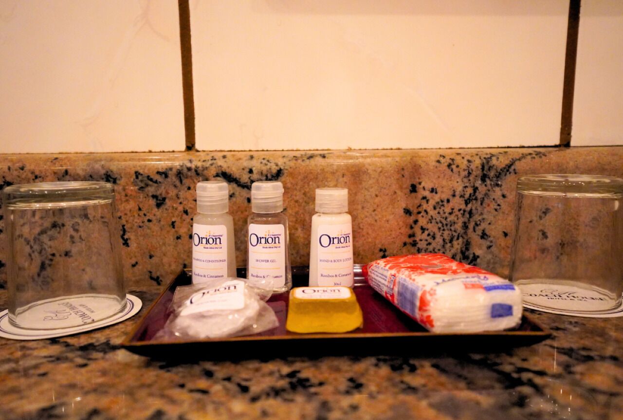 En bordplade med toiletartikler, heriblandt to flasker Orion brusegel, en sæbe, en lotion og en pakke toiletpapir.