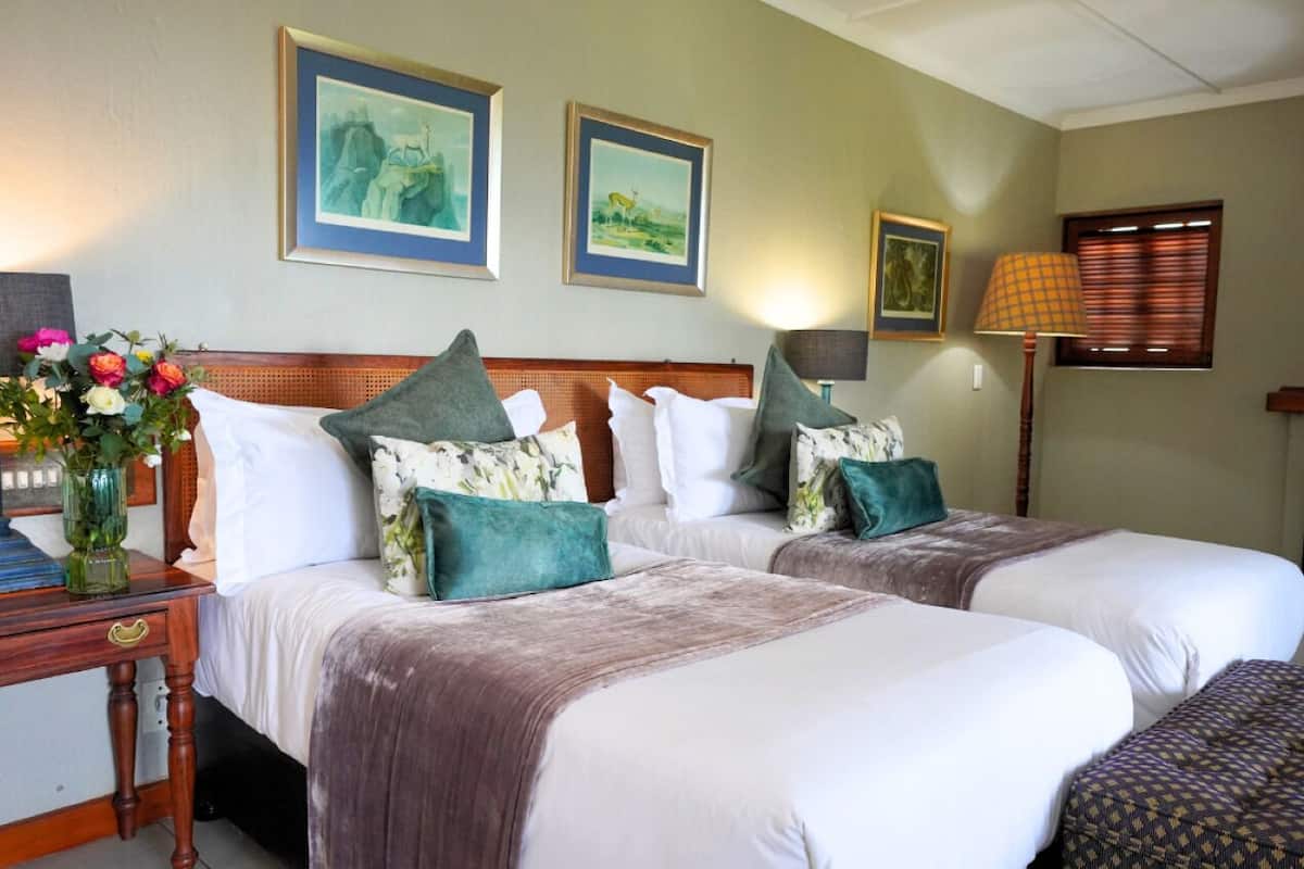 Ein Hotelzimmer mit zwei Betten, einem Nachttisch, einer Lampe und gerahmten Kunstwerken an der Wand.