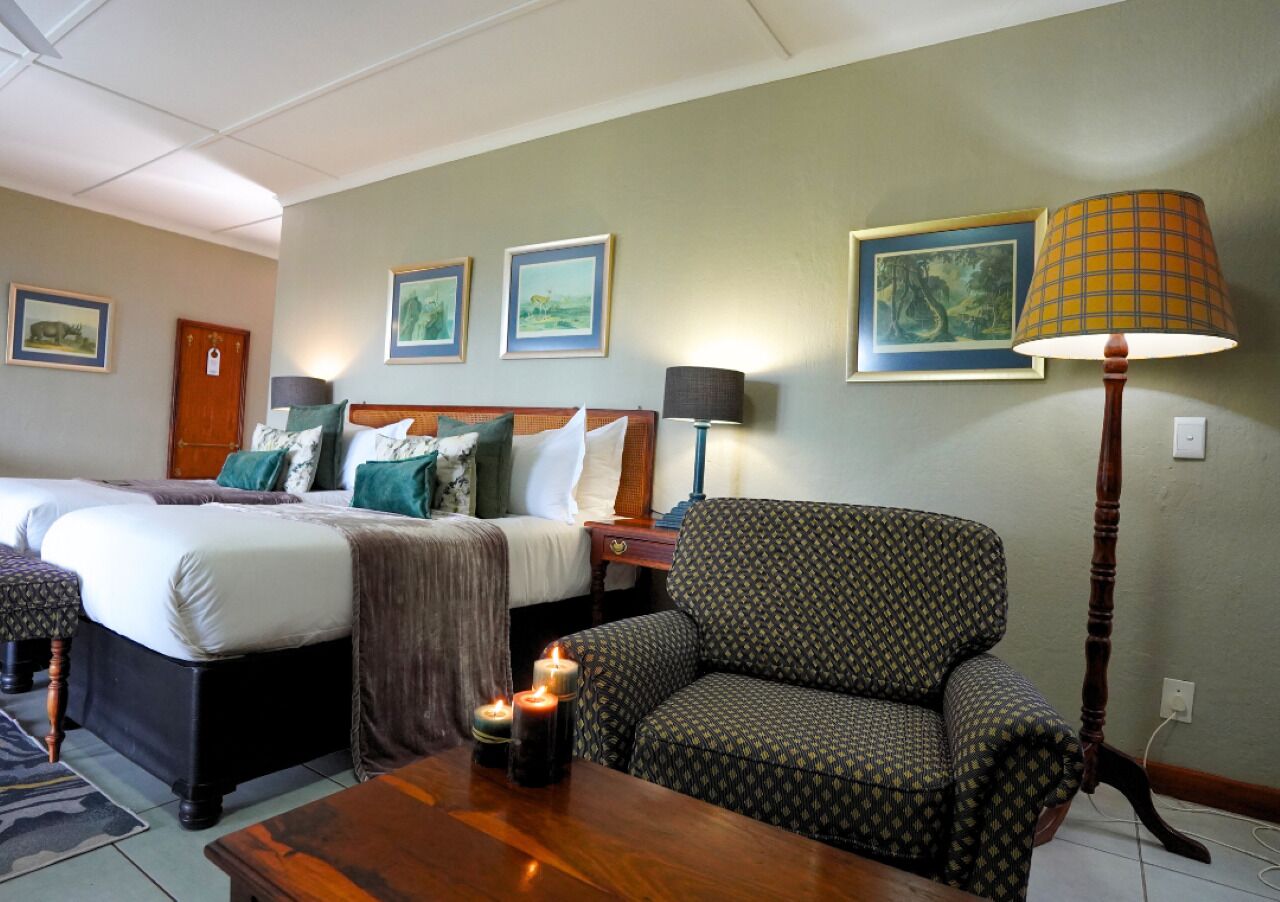 Ein Hotelzimmer mit zwei Betten, einem gemusterten Sessel, einem Holztisch mit Kerzen und gerahmten Bildern an den Wänden.