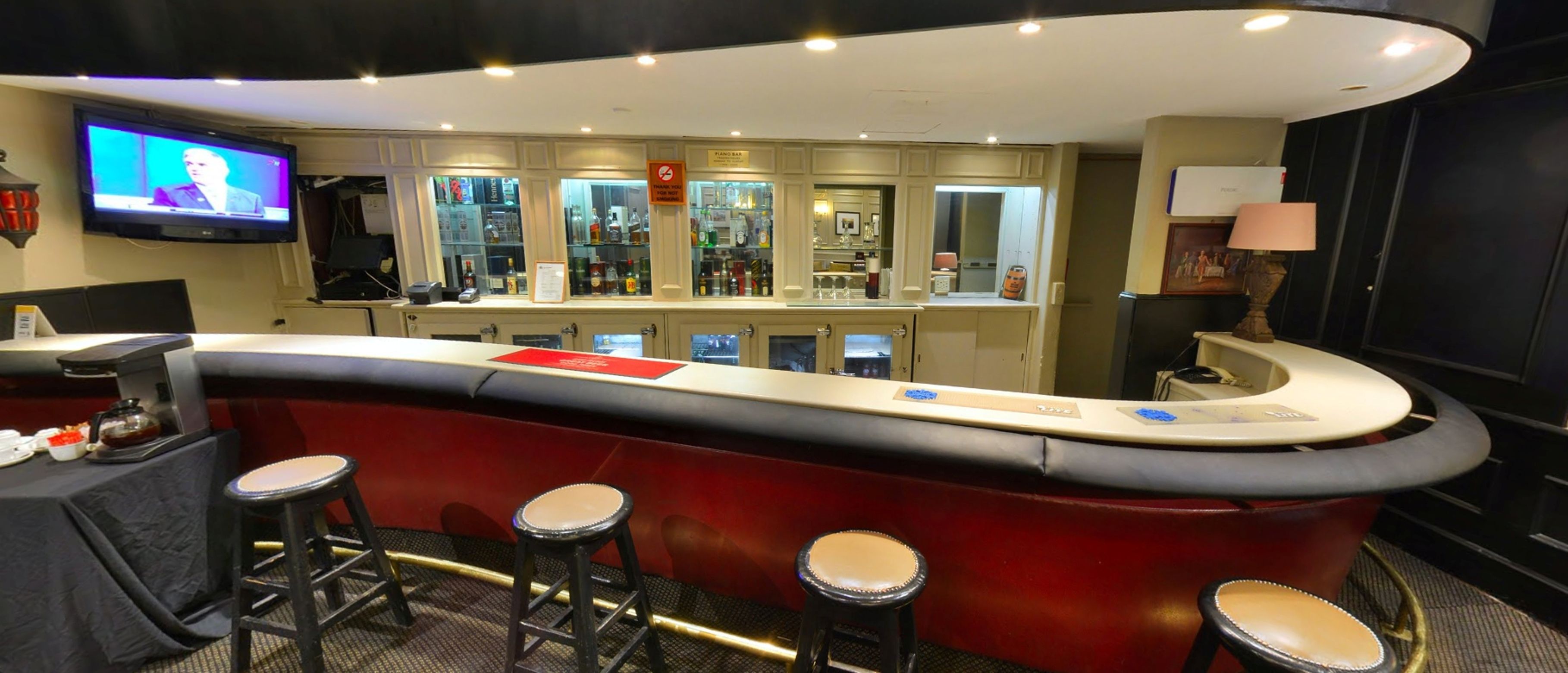 A bar area with stools, a television, and a bar counter with a piano bar sign.