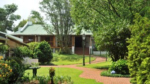 A traditional building with a green roof, surrounded by lush greenery and a brick pathway. - Coach House Hotel & Spa (Tzaneen)