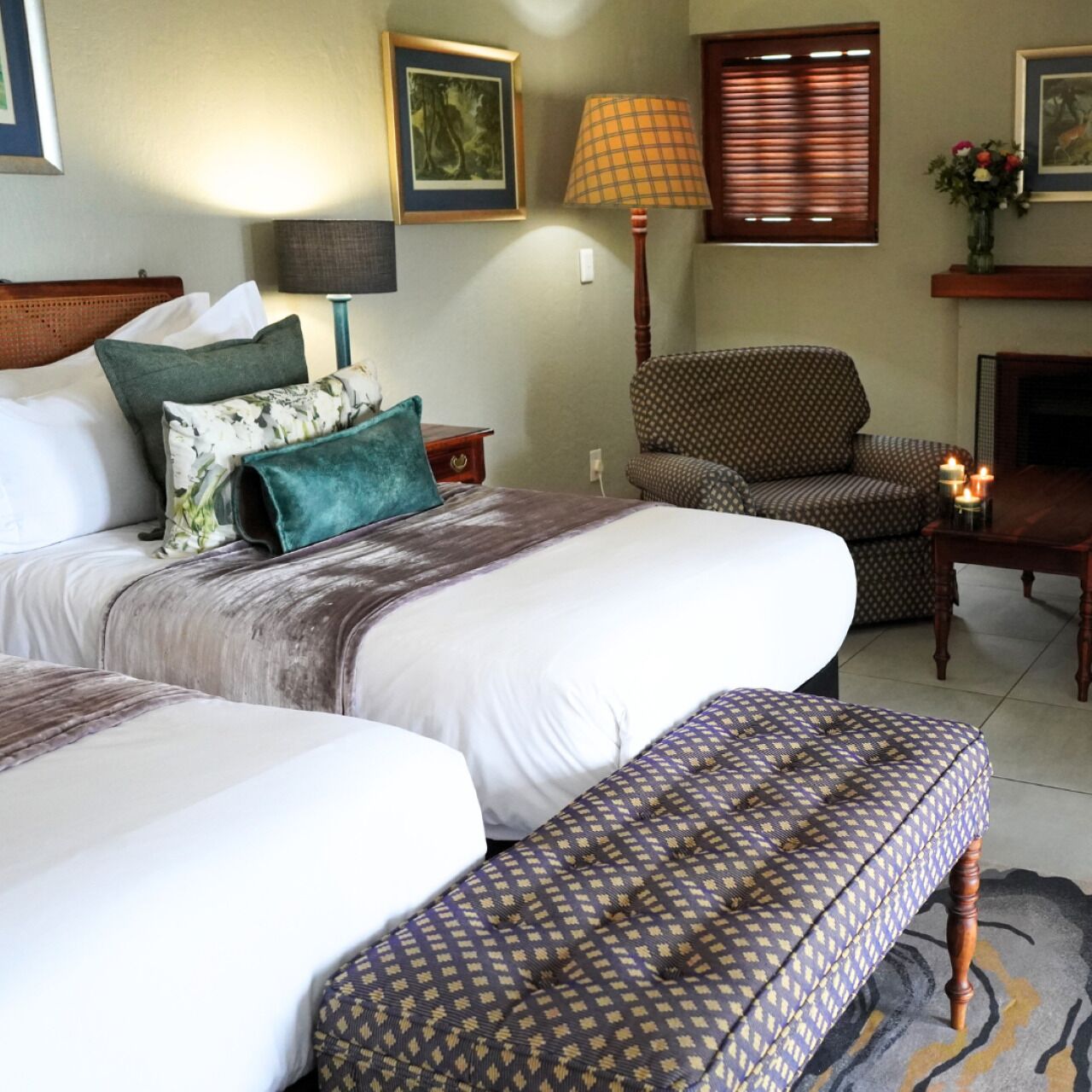 Een hotelkamer met twee bedden, een gestreept fauteuil, een kleine tafel met kaarsen en een open haard.