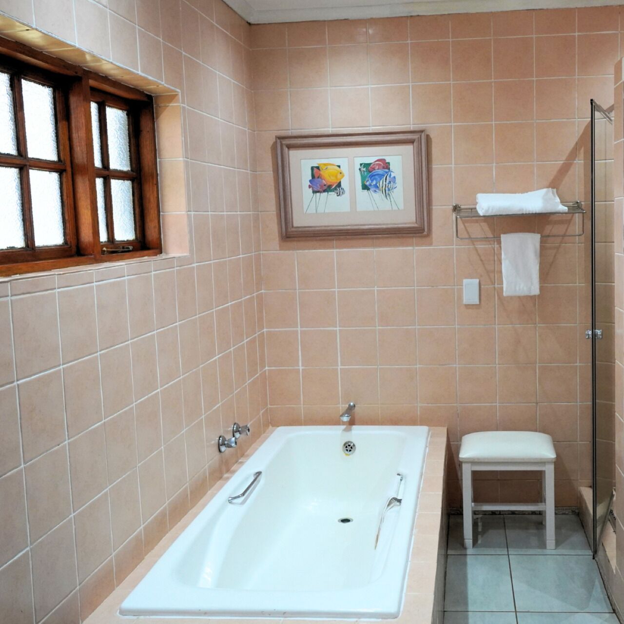 A bathroom with a bathtub, a small stool, a framed artwork on the wall, and a window with frosted glass.