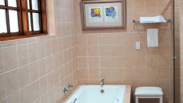 A bathroom with a bathtub, a small stool, a framed artwork on the wall, and a window with frosted glass.