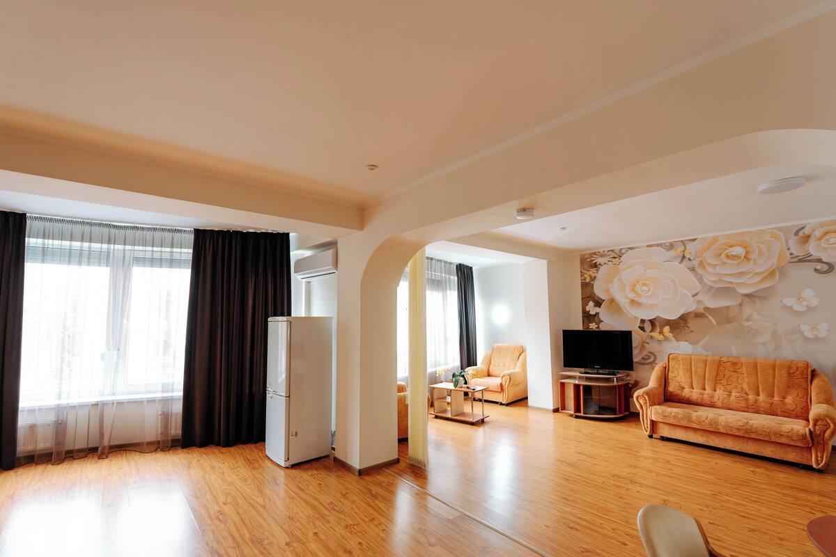 A spacious living room with a wooden floor, a sofa, a television, and a refrigerator.