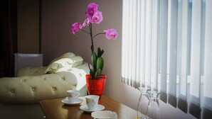 Een hotelkamer met een bed, een tafel met kopjes en schotels, en een rode vaas met een plant.