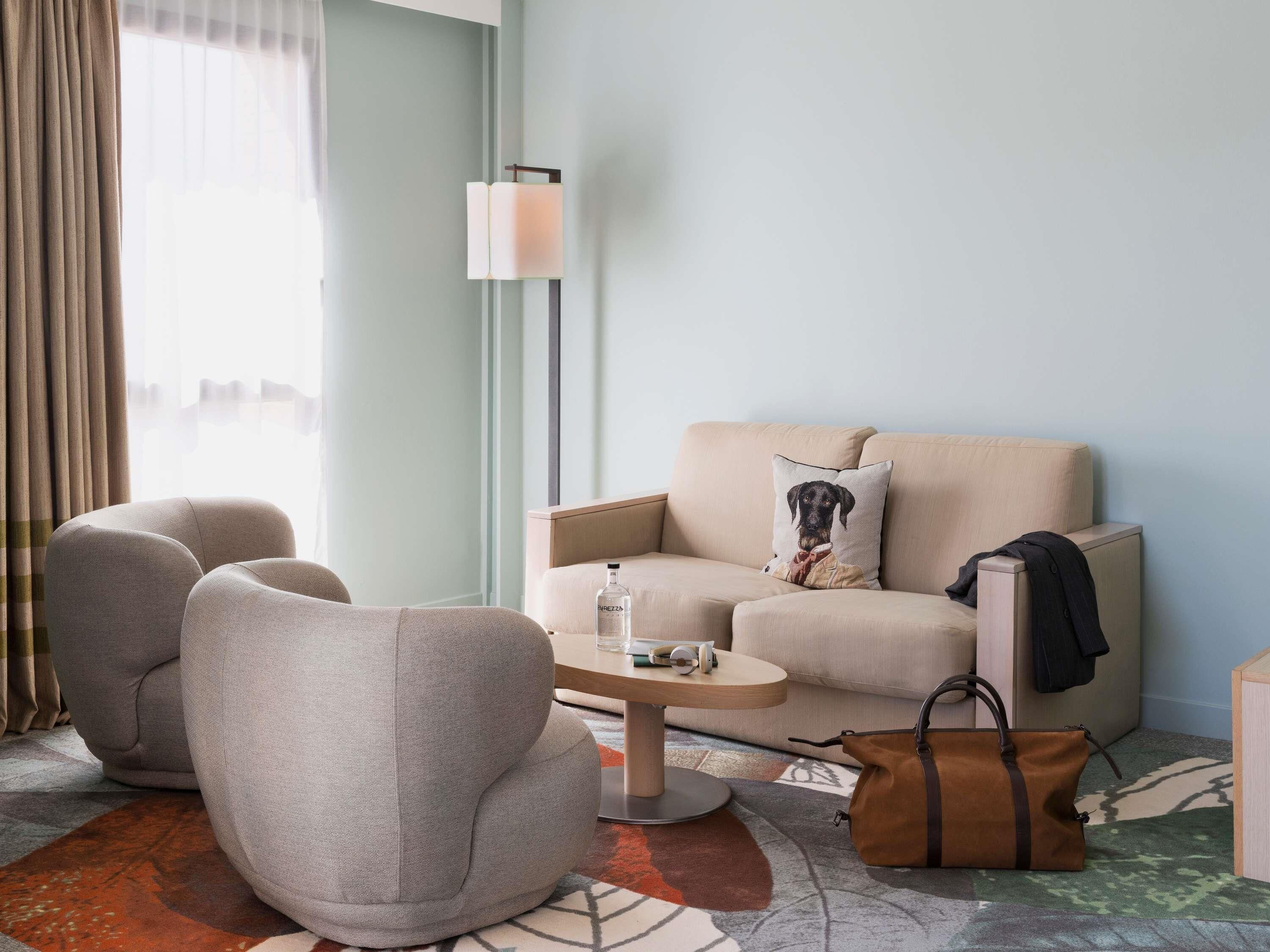 Una habitación de hotel moderna con sofá, sillón y una mesita con una botella.