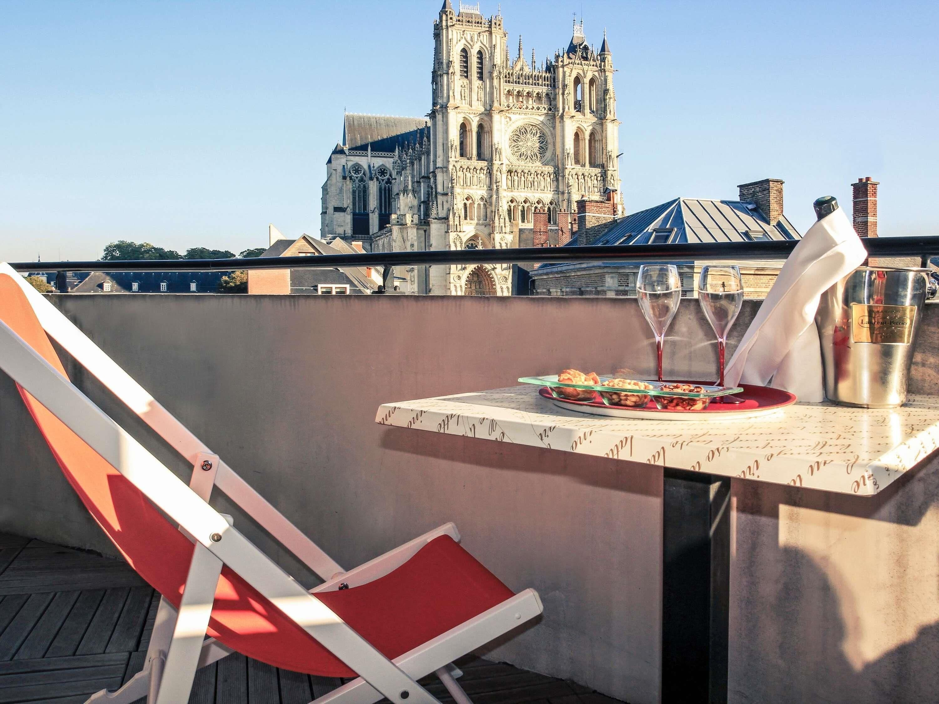 A balcony with a table set for two, a red chair, and a view of a historic cathedral in the background.