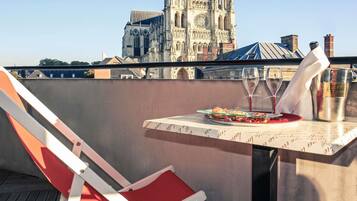 A balcony with a table set for two, a red chair, and a view of a historic cathedral in the background.