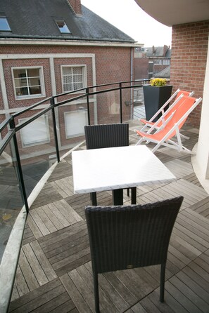 Un balcón con mesa y sillas, una planta en maceta y vistas a un edificio de ladrillo.