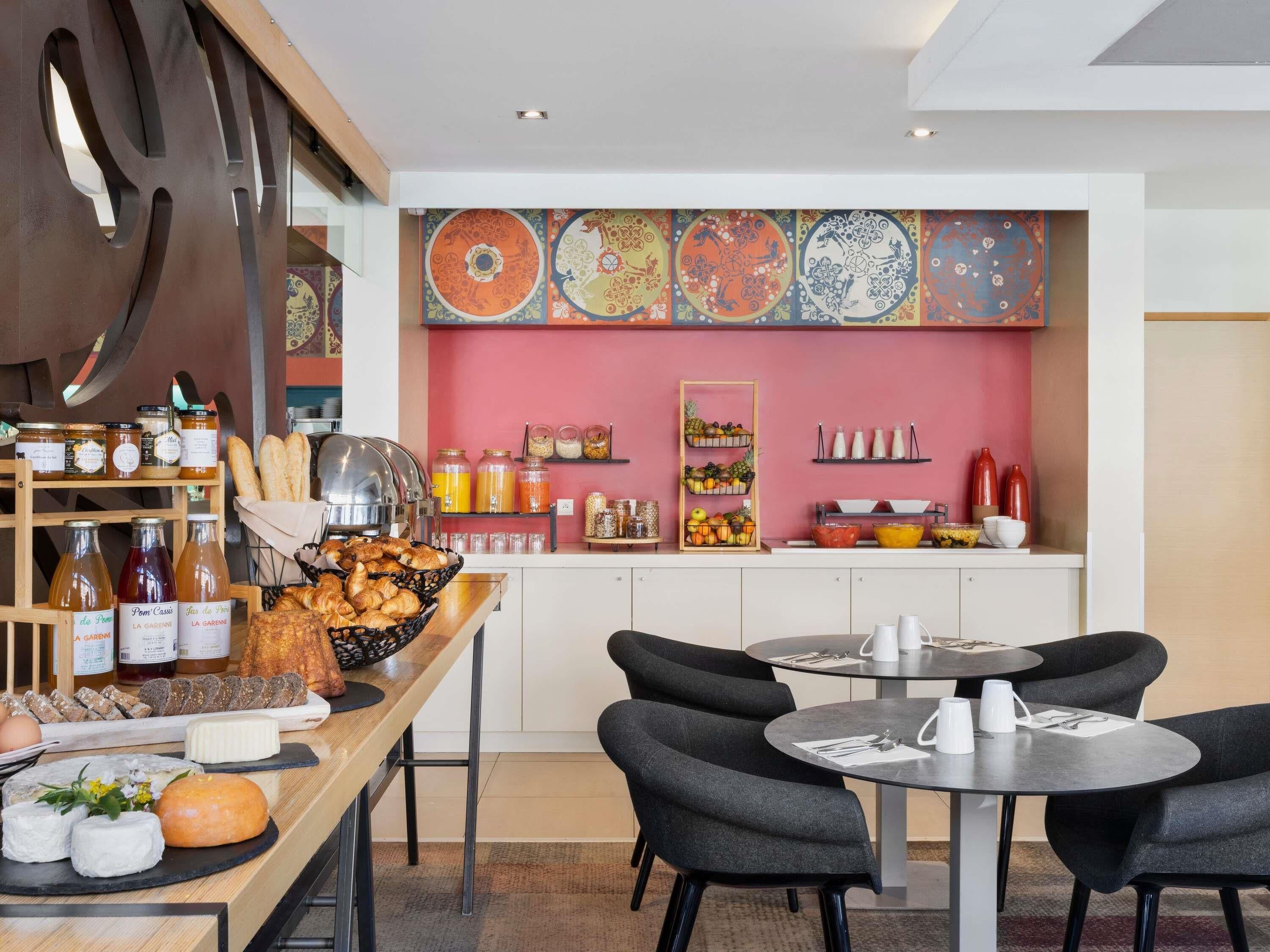 A breakfast buffet with various food items and beverages, a seating area with tables and chairs, and a colorful wall with decorative plates.