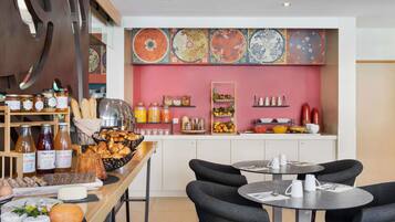 A breakfast buffet with various food items and beverages, a seating area with tables and chairs, and a colorful wall with decorative plates.
