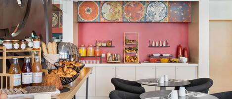 A breakfast buffet with various food items and beverages, a seating area with tables and chairs, and a colorful wall with decorative plates.