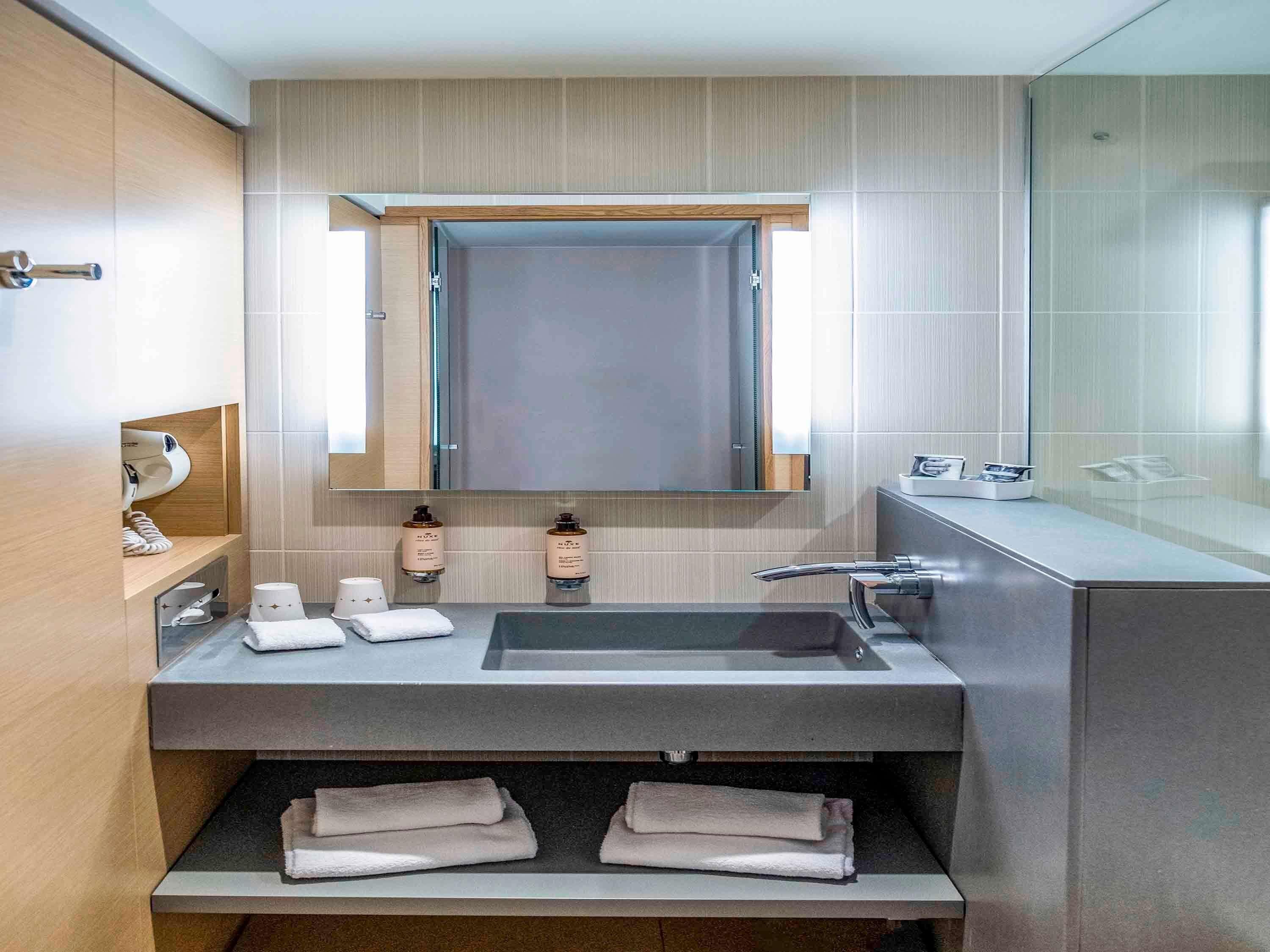 A modern bathroom with a large mirror, a sink, and a towel rack.