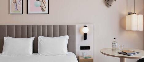 Une chambre d’hôtel comprenant un lit, une table de chevet, une table avec une chaise et des œuvres d’art accrochées au mur.