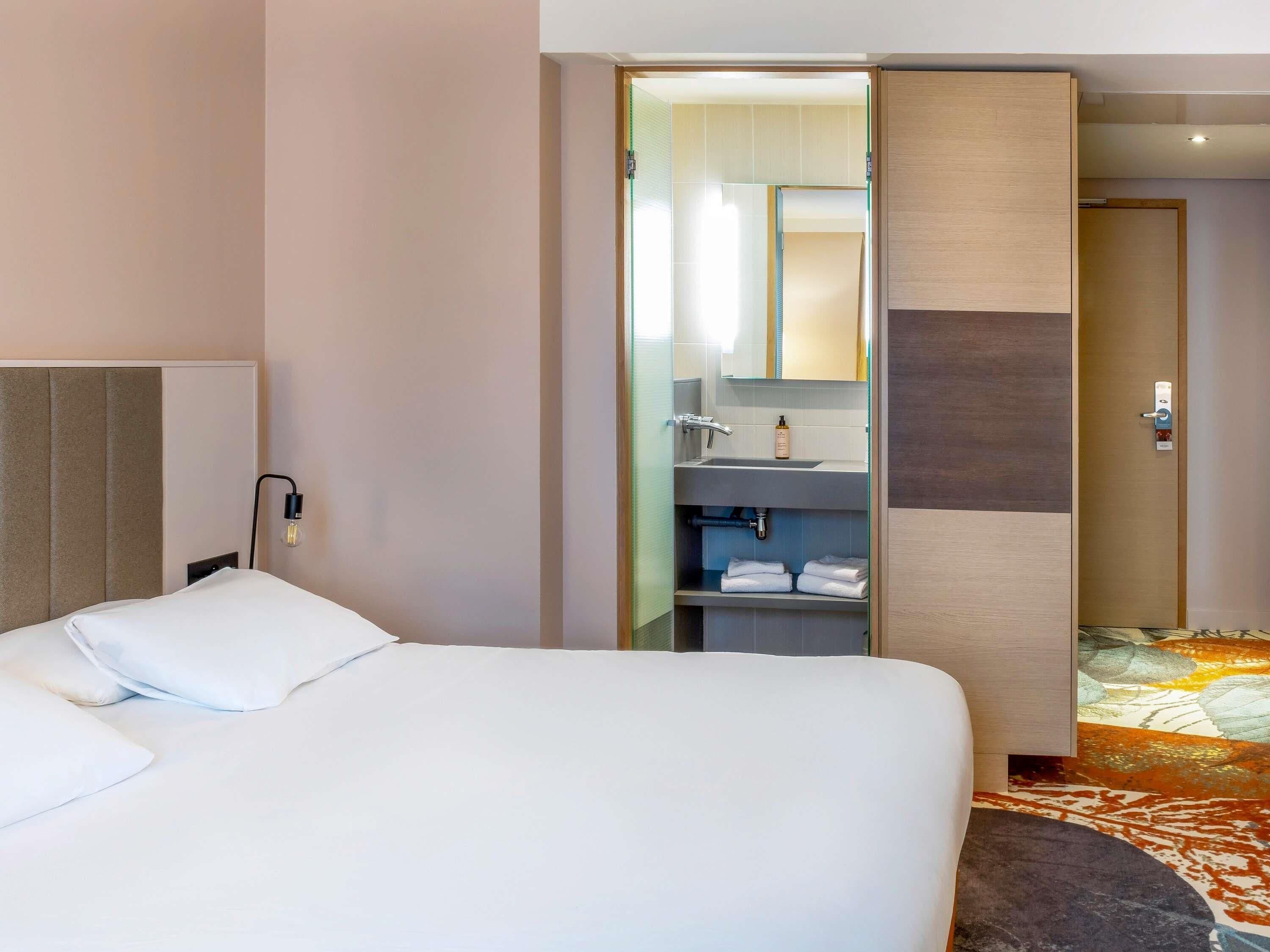 A hotel room with a bed, a bathroom with a sink and mirror, and a door leading to another room.