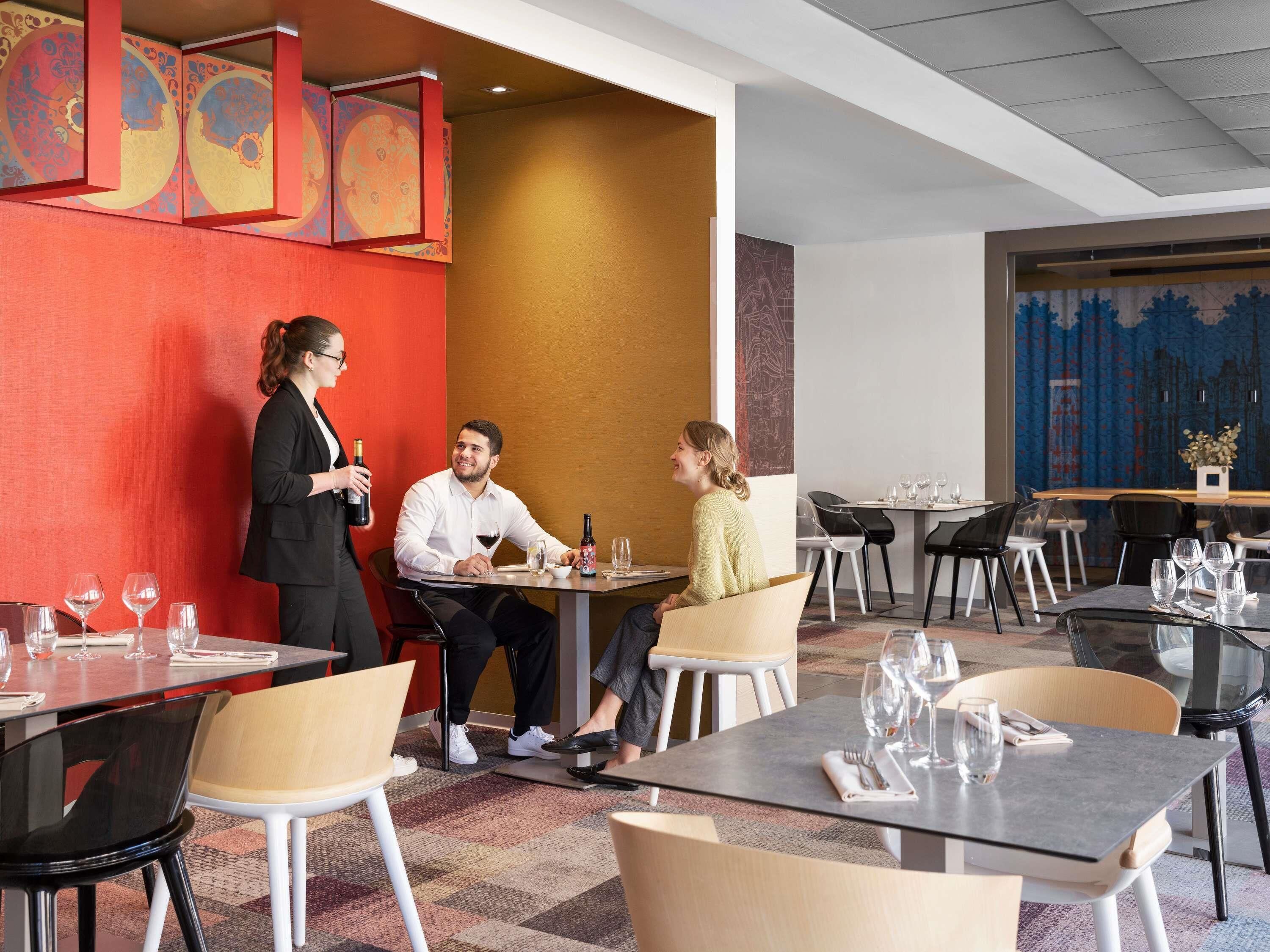 A modern restaurant with a vibrant red wall, a large mural, and a mix of black and white chairs.